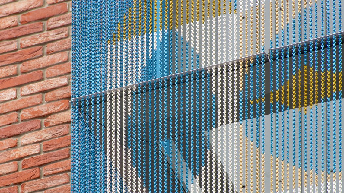 Détail matière – Maillons aluminium anodisés Kriskadecor - <p>Gros plan sur la matière Kriskadecor : maillons aluminium anodisés bleus, or et blancs. L’image révèle la lecture pixelisée du motif et la performance du matériau pour les façades extérieures personnalisées.</p>