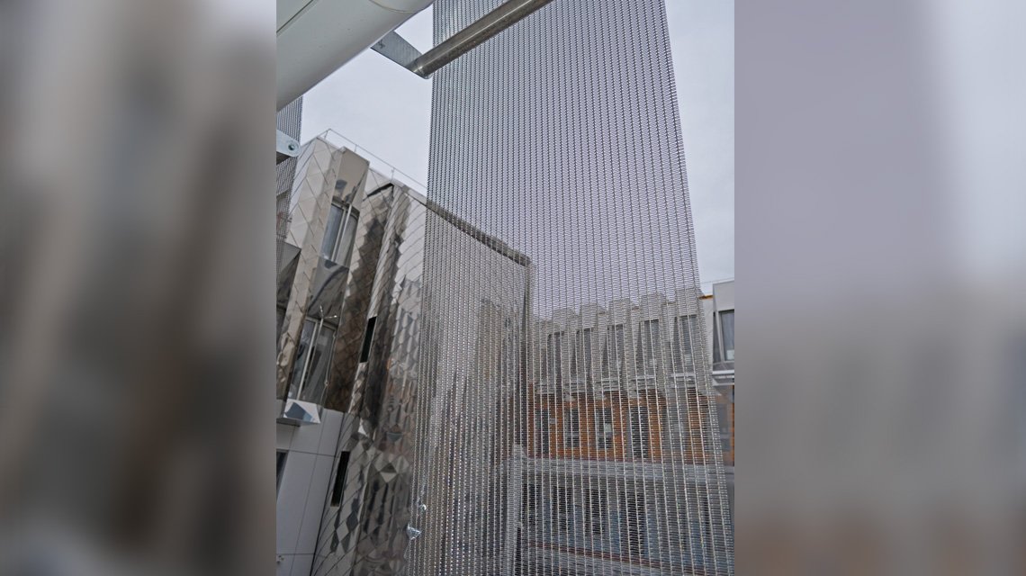 Maille métallique SATURN en acier inoxydable mise en oeuvre en façade d'un bâtiment de logements à Paris - <p>maille métallique câblée appelée SATURN fabriquée sur mesure en acier inoxydable 316L et mise en oeuvre en bandeaux, en panneaux zig zag sur la façade du bâtiment de logements. La maille métallique allie esthétique et fonctionnalité comme brise-soleil.</p>