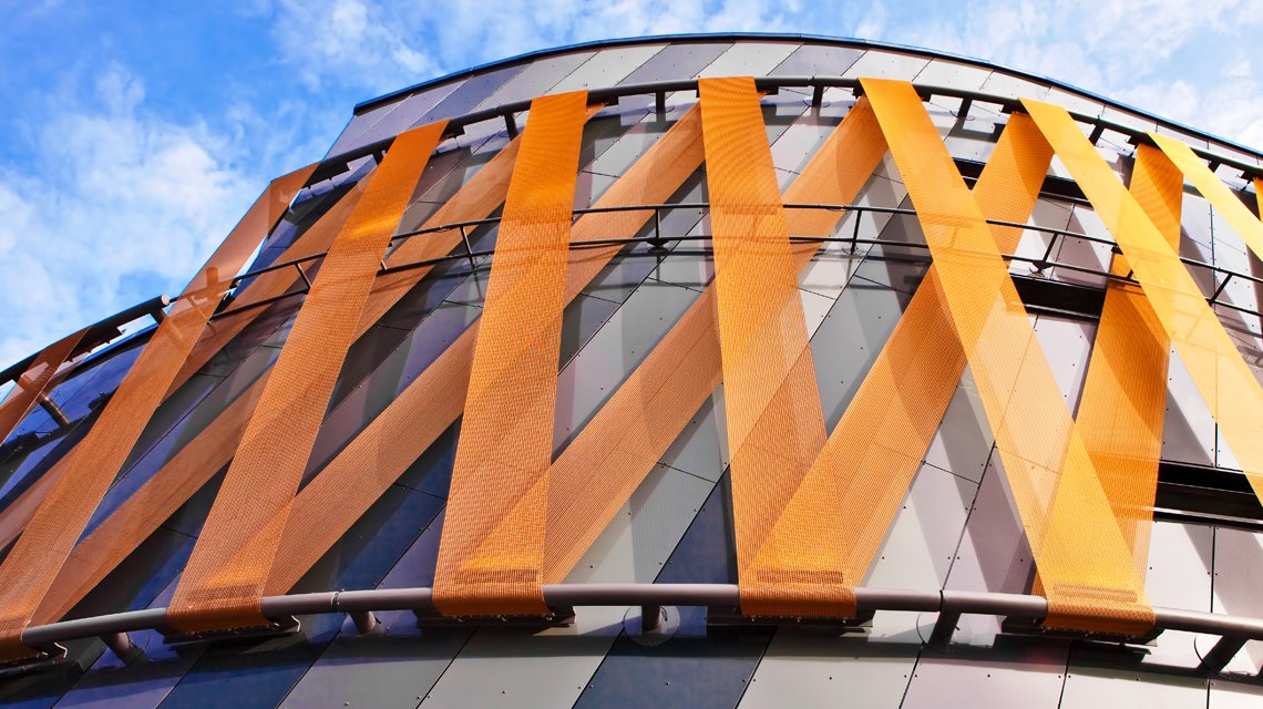 Bandes de maille métallique câblée colorée SATURNP05140 en façade architecture sur mesure www.maillemetaldesign.fr - <p>façade moderne d’un centre commerciale revêtue de bandeaux de maille métallique câblée. La maille métallique STAURN est composée de câbles inox et de tiges métallique inox recouvertes d’une couche de peinture plastifiée.</p>