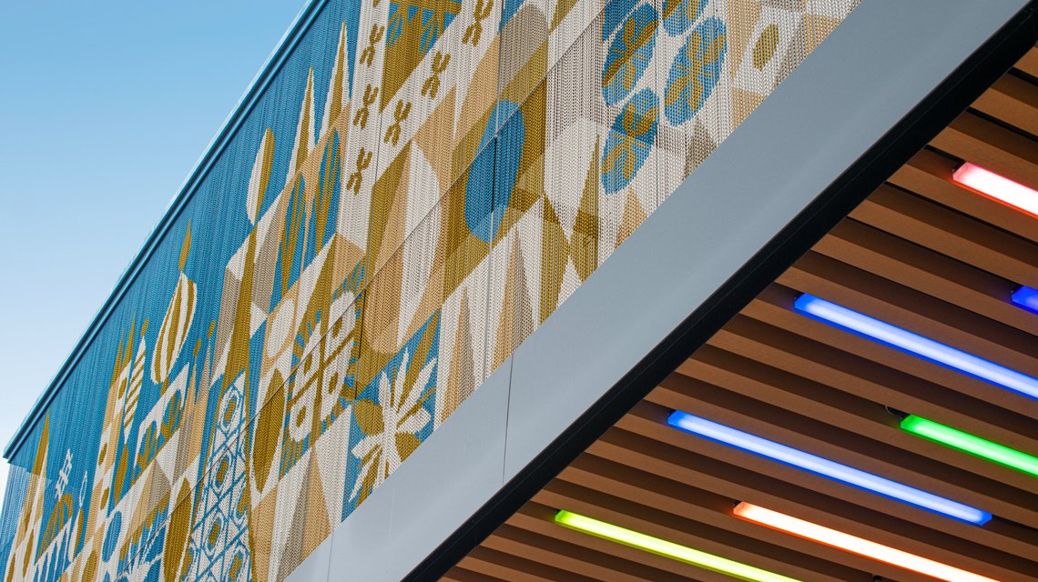 Façade Kriskadecor Disney Village – Vue sous auvent lumineux - <p>Vue dynamique de la façade Kriskadecor prise depuis l’auvent coloré du Disney Village. La photo souligne l’intégration du rideau de chaînes aluminium dans un environnement retail vivant et lumineux.</p>