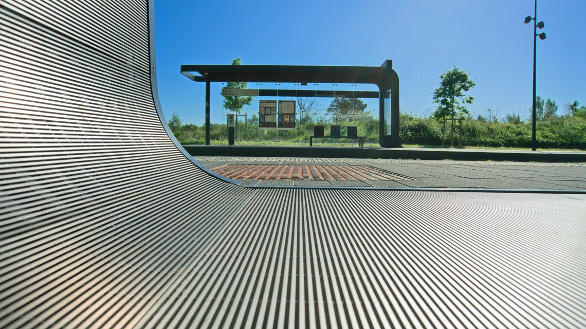 Caillebotis slot cintré – Continuité architecturale Tram 12 - <p>Caillebotis en slot inox AISI 316L cintré sur mesure, assurant une continuité esthétique entre l’habillage vertical des abris et les zones de circulation. Une solution architecturale durable adaptée à l’aménagement urbain et aux infrastructures de transport public.</p>