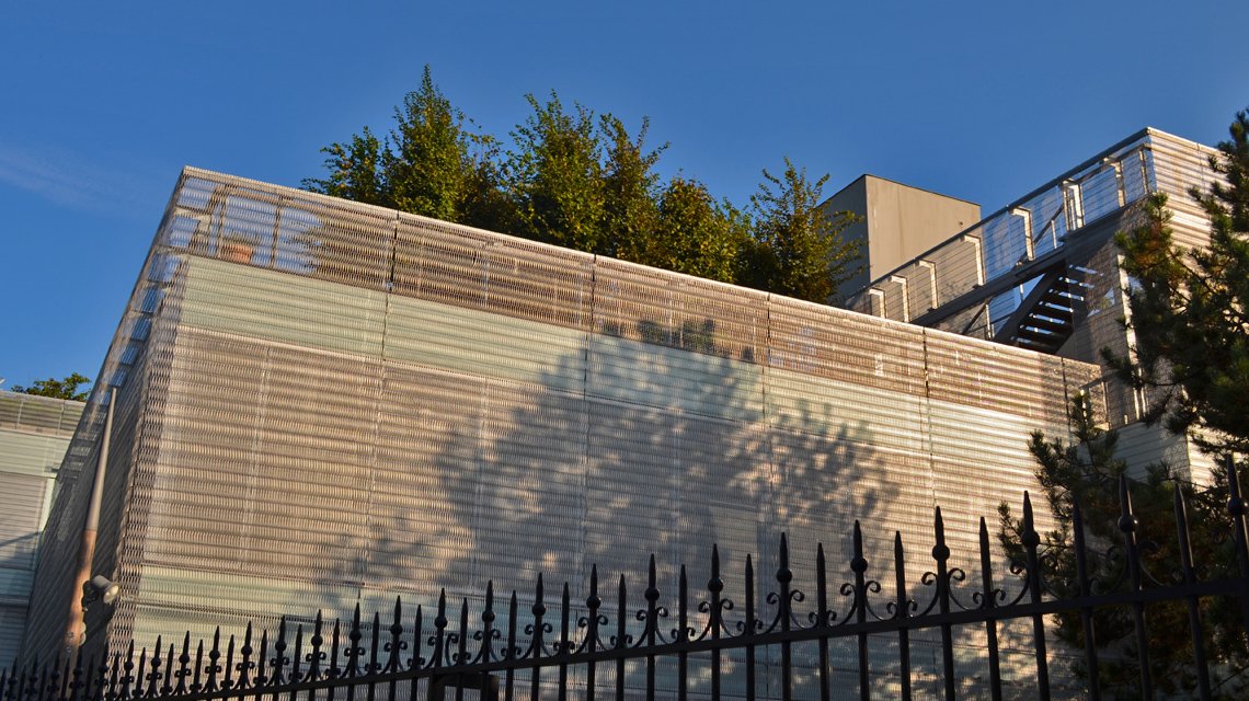 Façade en maille inox – Intégration paysagère Roland Garros - <p>Vue d’ensemble d’un bâtiment enveloppé de maille métallique spiralée EIFFEL30150, intégrée harmonieusement à la végétation entourant le site de Roland Garros, créant un dialogue entre architecture et nature.</p>