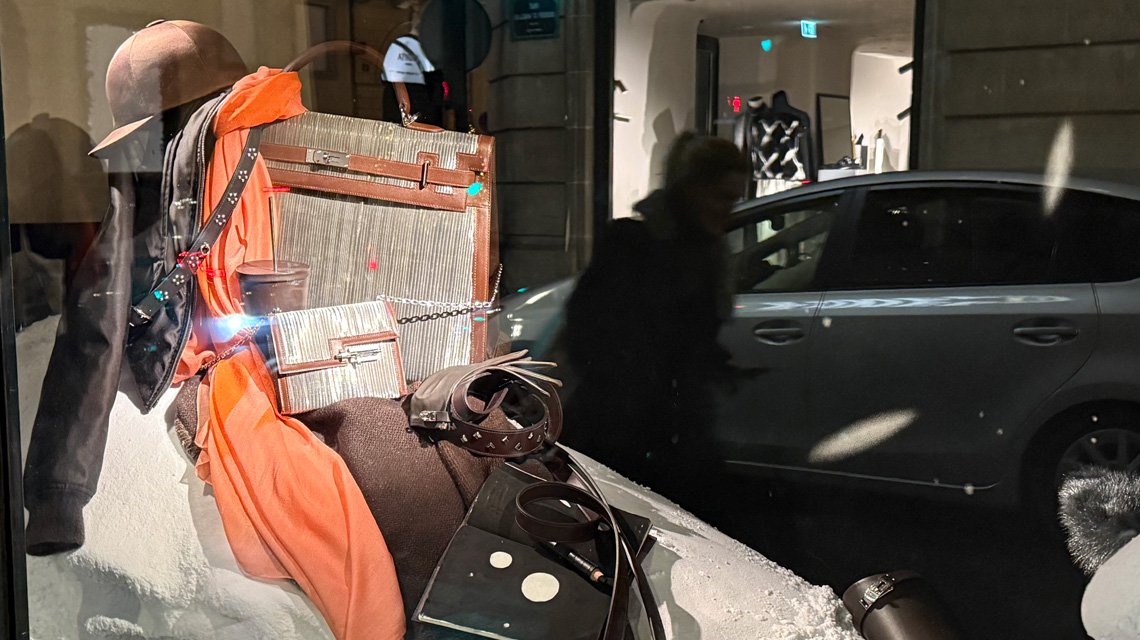 Scénographie Hermès – sac et étole avec détails en maille métallique Aura Inox - <p>Zoom sur la mise en scène de la vitrine Hermès : étole orange drapée, sac habillé de maille métallique Aura Inox et accessoires présentés dans une composition raffinée. Une ambiance chaleureuse et poétique, typique de la Maison.</p>