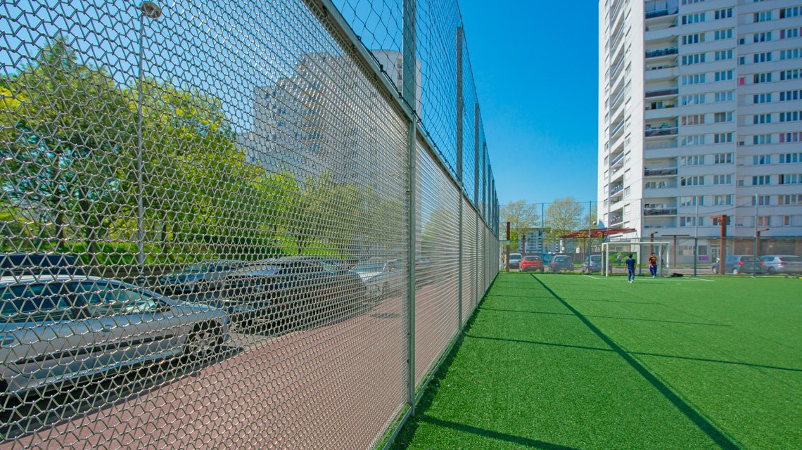 Clôture sur mesure en maille métallique spiralée en acier inoxydable pour le city stand d'Alfortville - <p>Réalisés sur mesure, les panneaux en résille métallique spiralée, modèle Torroja-R de notre partenaire Codina Architectural, définissent avec justesse les contours du terrain, tout en laissant circuler la lumière, les regards et l’air. <br class='autobr' />
Leur trame régulière accompagne les lignes du site et s’efface dans le paysage, offrant une présence discrète, presque immatérielle.</p>